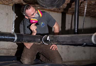 A home inspector inspecting plumbing in a crawlspace.